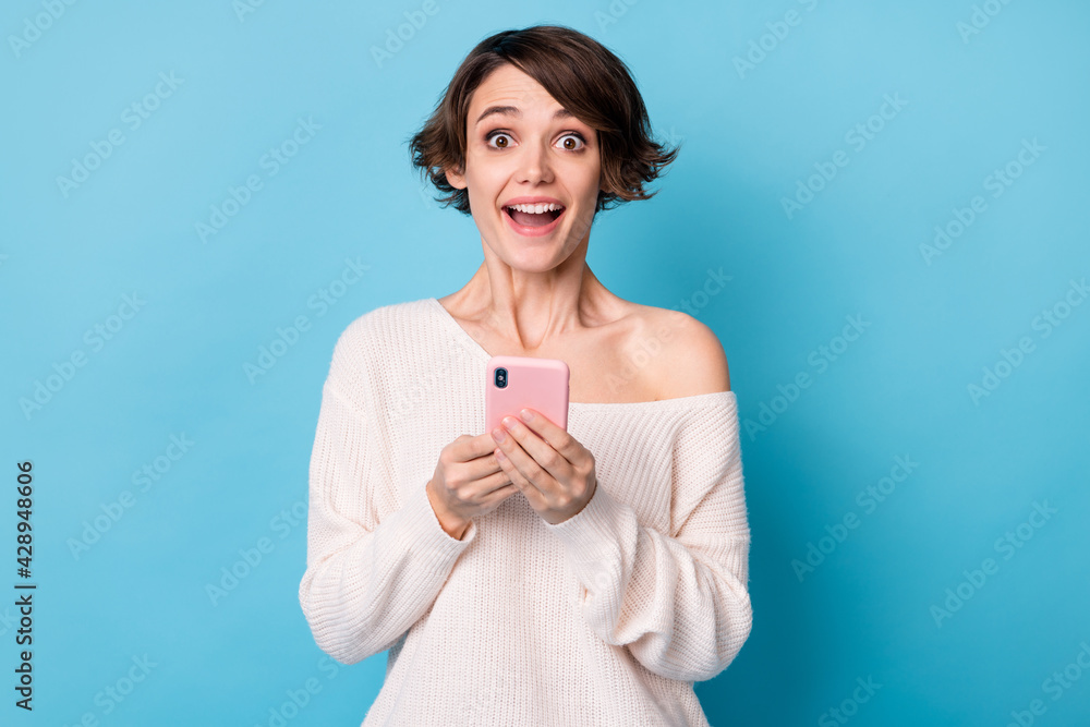 Photo portrait of cheerful excited girl holding phone in two hands isolated on pastel blue colored background Photo portrait of cheerful excited girl holding phone in two hands isolated on pastel blue colored background