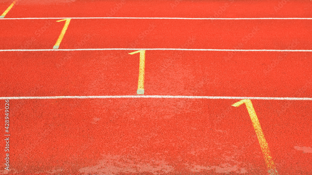 Side view of red running tracks in a street stadium. White and yellow rubberized treadmill markings.