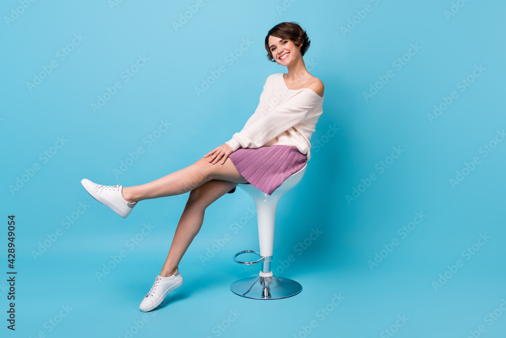 Photo portrait full body view of cute girl raising leg sitting on bar stool isolated on pastel blue colored background