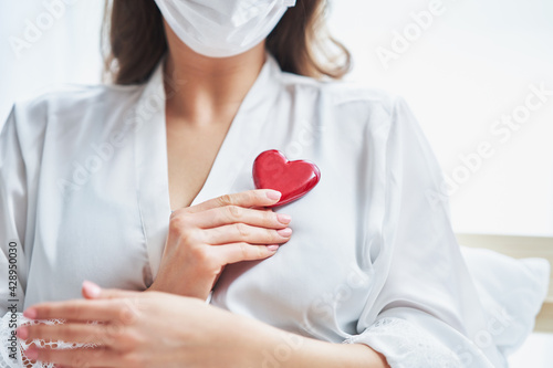 Adult woman in mask showing heart shape at home Covid-19 concept