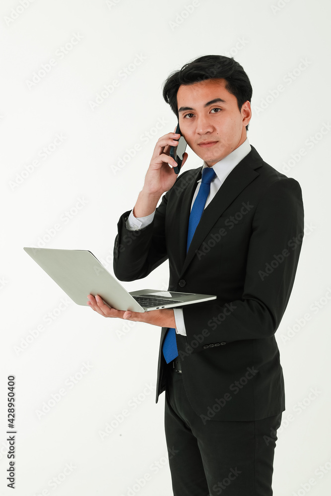 A smart young asian businessman or entrepreneur wearing formal black suit standing over white background, holding and looking at laptop notebook computer and look at screen. A smart young asian businessman or entrepreneur wearing formal black suit standing over white background, holding and looking at laptop notebook computer and look at screen.