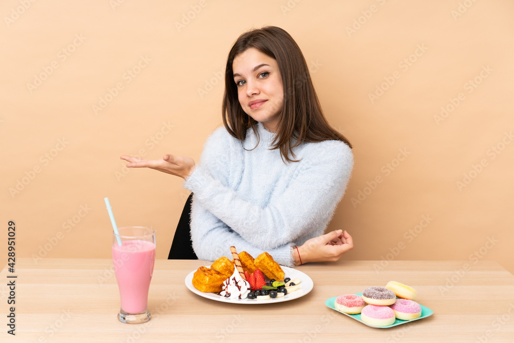 Teenager girl eating waffles isolated on beige background presenting an idea while looking smiling towards