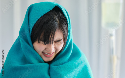 Murais de parede Close-up of a severe sick young woman sitting on bed in the hospital, got a flu or cold and covered her body in green blanket to relieve from a frozen fever