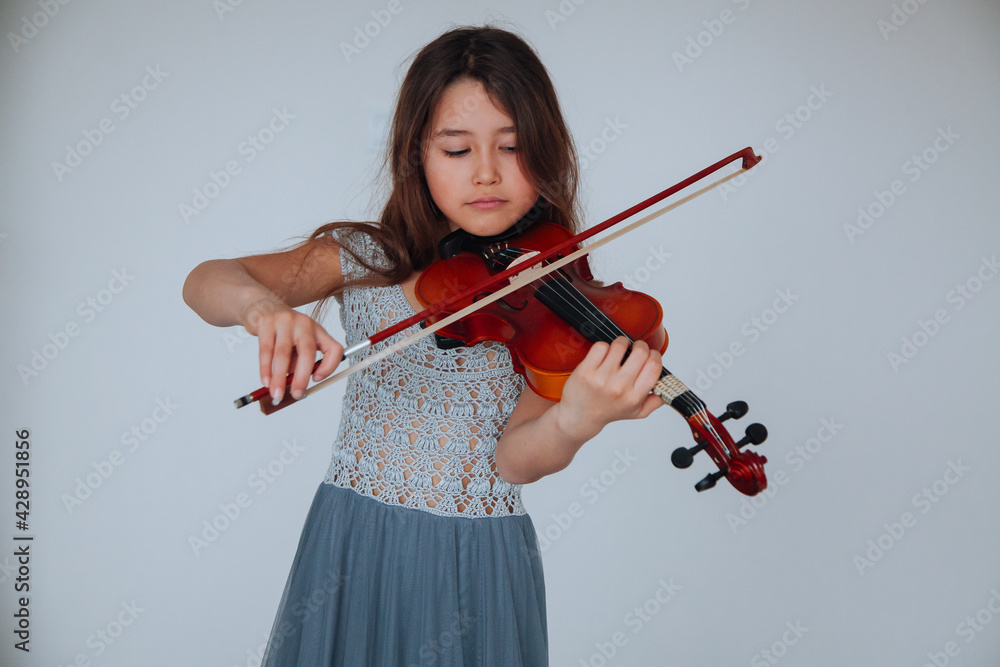 Little brunette girl in a beautiful dress playing violin indoors. Music instruments concept. Little brunette girl in a beautiful dress playing violin indoors. Music instruments concept.