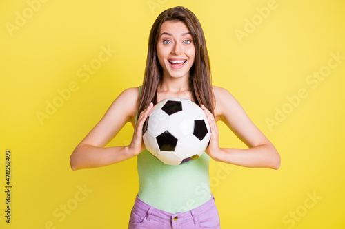 Photo of young beautiful happy smiling girl with long brown hair hold football ball isolated on yellow color background © deagreez