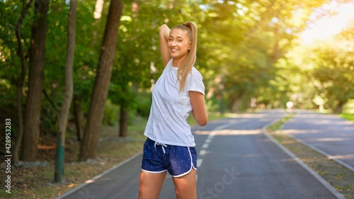 Woman runner stretching arms before exercising summer park morning