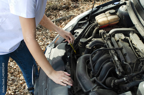 the girl checks the oil under the hood of the car
