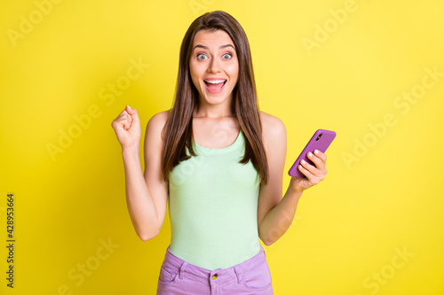 Photo of amazed crazy lady hold telephone raise fist wear green singlet isolated yellow color background