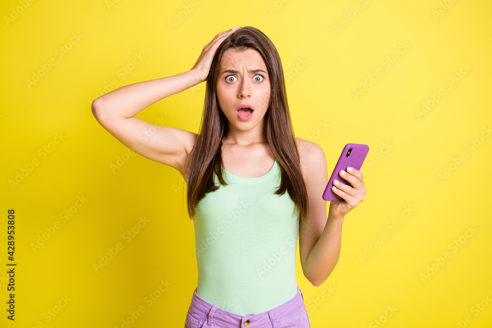 Photo of young attractive lovely amazed surprised girl see bad comment in phone isolated on yellow color background Photo of young attractive lovely amazed surprised girl see bad comment in phone isolated on yellow color background