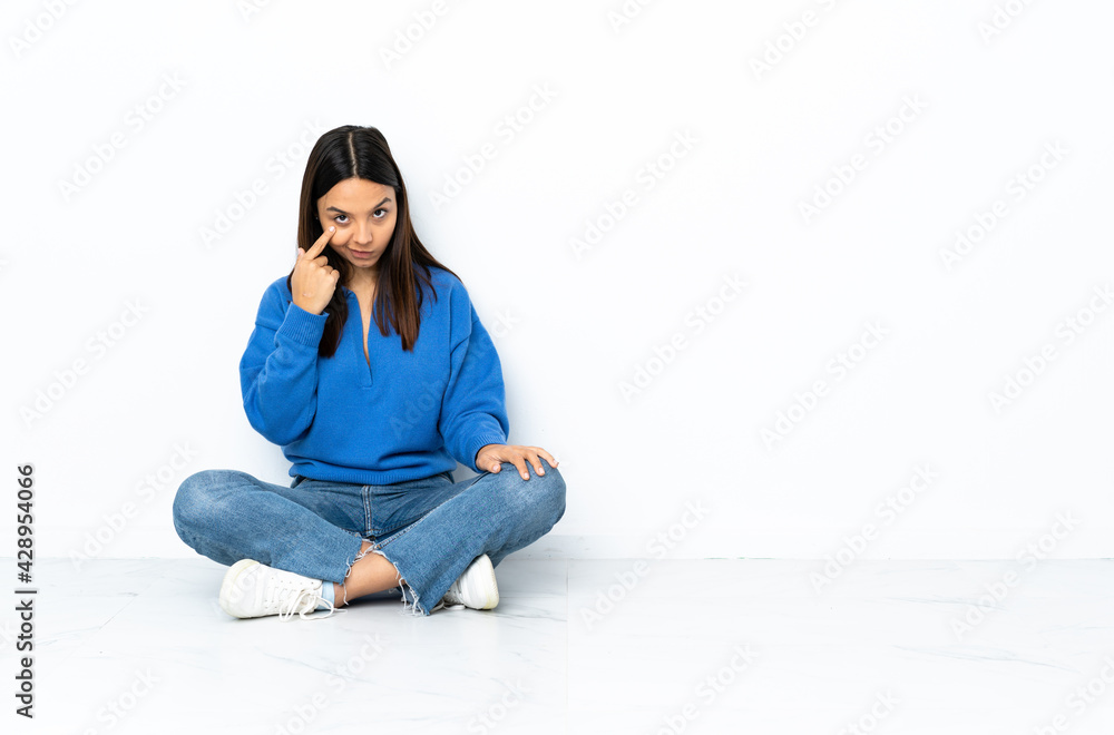 Young mixed race woman sitting on the floor isolated on white background showing something Young mixed race woman sitting on the floor isolated on white background showing something