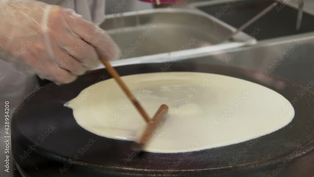 cook is baking thin pancakes, pouring dough on hot cooker and leveling up, closeup view cook is baking thin pancakes, pouring dough on hot cooker and leveling up, closeup view