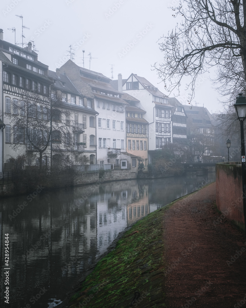 Beautiful view of the houses in a row in Strasbourg standing at river Rhein. Mystic foggy weather, autumn atmosphere. Fall season. European architecture.