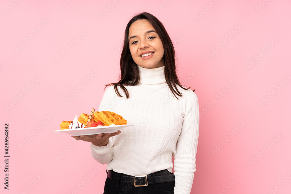 Young brunette woman holding waffles over isolated pink background laughing Young brunette woman holding waffles over isolated pink background laughing
