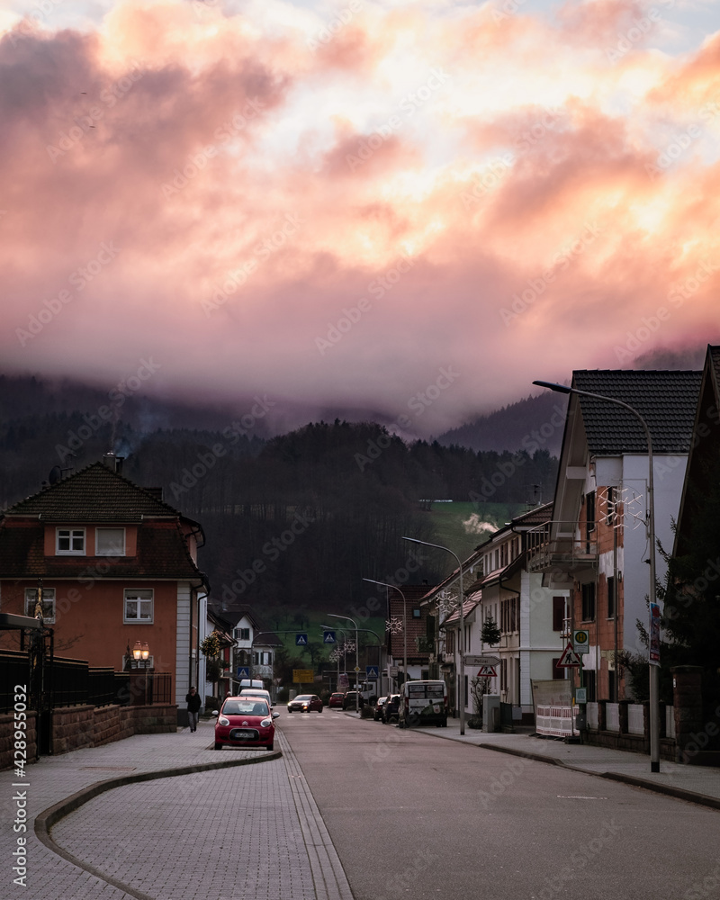 Beautiful view on the sunset in a small town in the Germany. Big mountains on the background. Fog and clouds hiding peak of the mountain. Schwarzwald nature