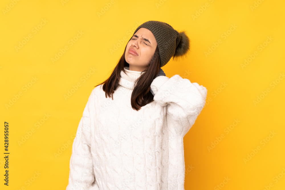 Young woman with winter hat over isolated yellow background with neckache Young woman with winter hat over isolated yellow background with neckache