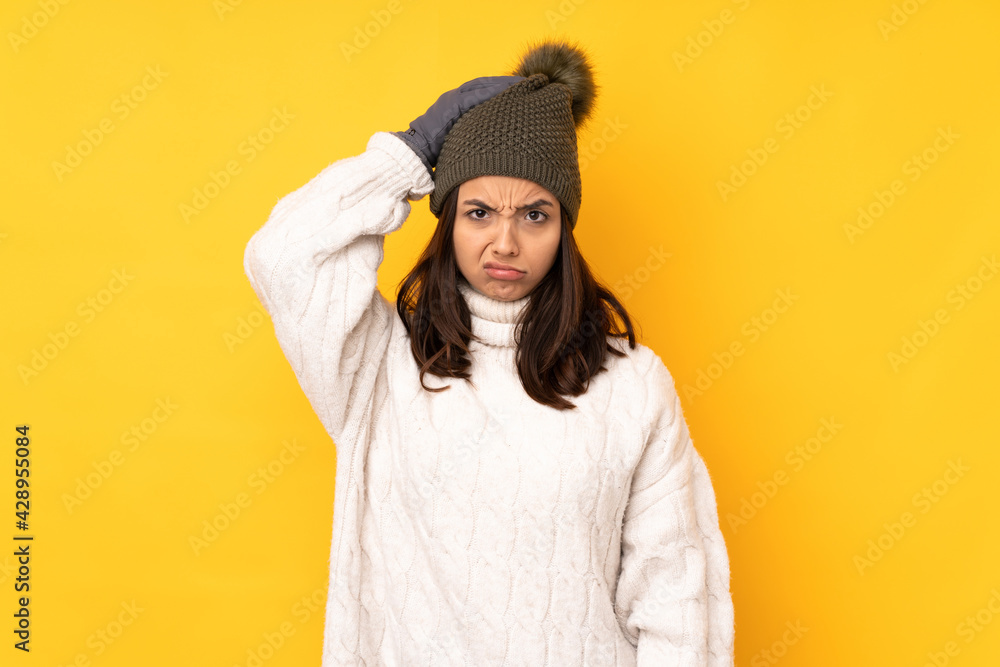Young woman with winter hat over isolated yellow background with an expression of frustration and not understanding Young woman with winter hat over isolated yellow background with an expression of frustration and not understanding