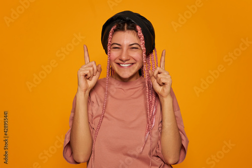 Foto Excited teenage girl wearing pink braids and facial piercing posing isolated wit