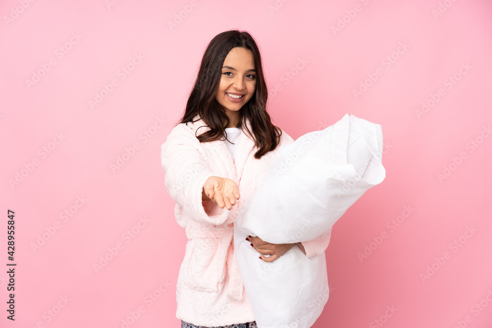 Young woman in pajamas isolated on pink background holding copyspace imaginary on the palm to insert an ad Young woman in pajamas isolated on pink background holding copyspace imaginary on the palm to insert an ad
