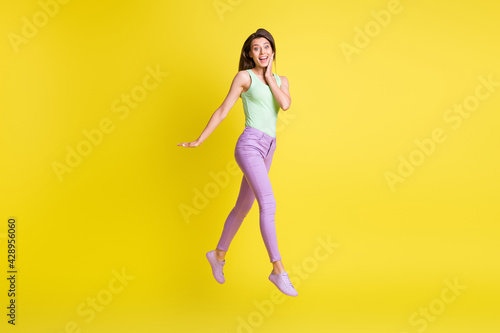 Photo of lady jump go hand face wear green top purple pants sneakers isolated yellow color background