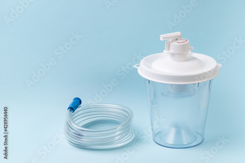 Plastic canister from medical suction machine on blue. Part of portable aspirator used to remove mucus, blood, bodily fluids from patient. Medical equipment using in ambulances and nursing homes