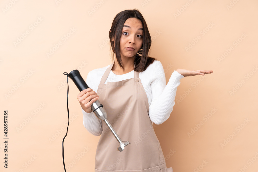 Young brunette girl using hand blender over isolated background unhappy for not understand something