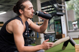 man drinking water and looking the phone at gym