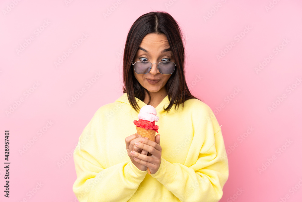 Young brunette girl holding a cornet ice cream over isolated pink background scheming something Young brunette girl holding a cornet ice cream over isolated pink background scheming something