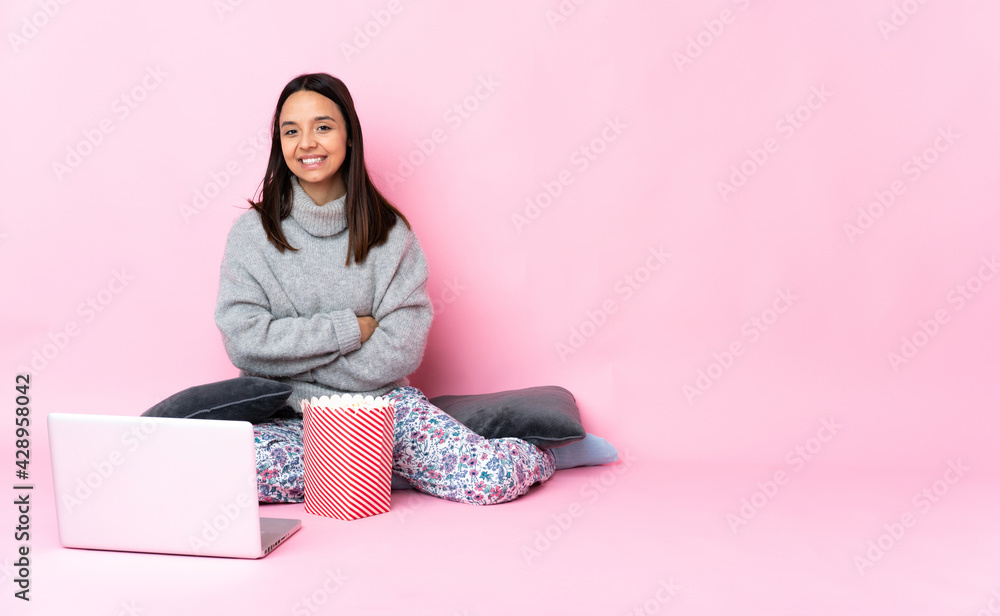 Young mixed race woman eating popcorn while watching a movie on the laptop with arms crossed and looking forward Young mixed race woman eating popcorn while watching a movie on the laptop with arms crossed and looking forward