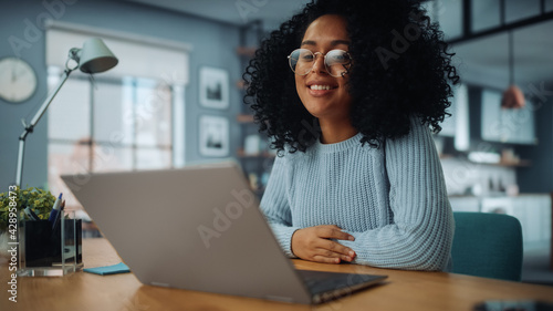 Portrait of Beautiful Authentic Latina Female in Cozy Living Room Making a Video Call on Laptop Computer at Home. Freelancer Chatting with Colleagues or Friends Over the Internet on Social Networks.