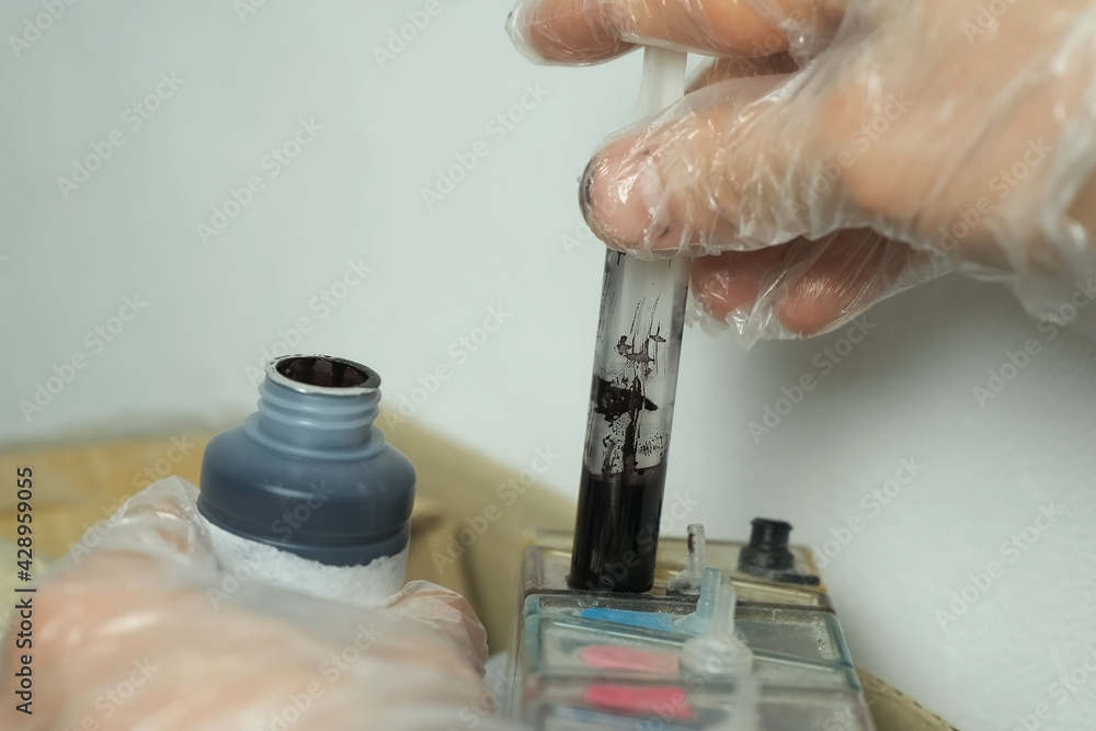 Man puts black ink in a printer using a syringe, hands in gloves ...