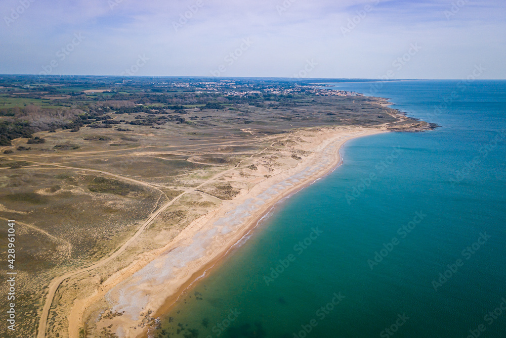 Aerial photography of sunny beach from above with clear water, sandy dunes behind and a small village in the background