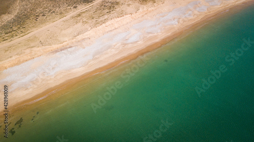 Aerial photography of sunny beach with part sand and part stones from above with clear water with a diagonale composition