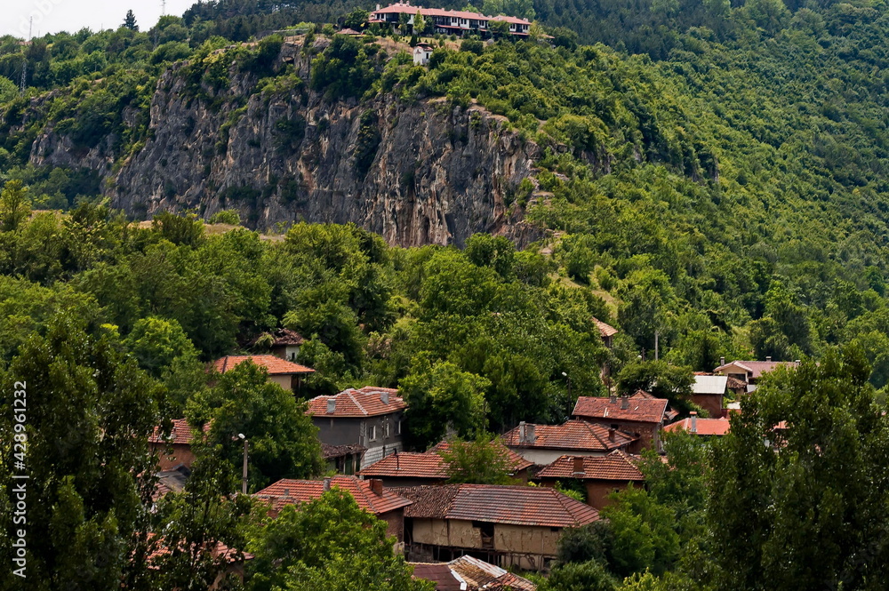 View of the beautiful village of Cherven village, Bulgaria, located below, above and in the high limestone cliffs, protected by magnificent deciduous trees   