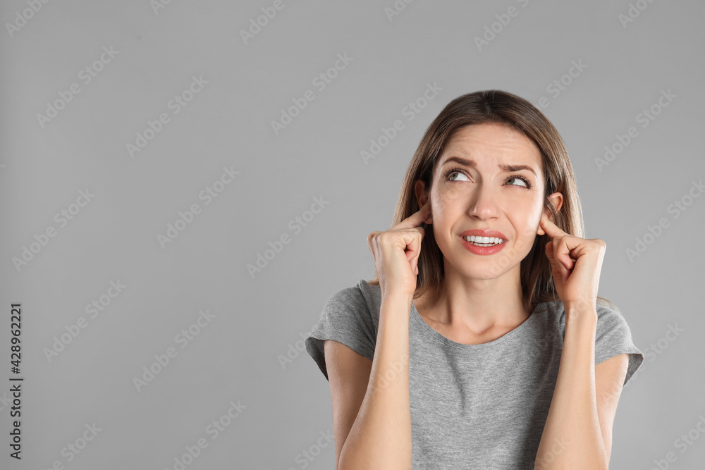 Emotional young woman covering her ears with fingers on grey background. Space for text Emotional young woman covering her ears with fingers on grey background. Space for text