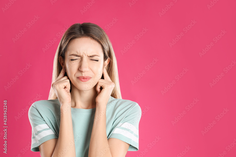 Emotional young woman covering her ears with fingers on pink background. Space for text Emotional young woman covering her ears with fingers on pink background. Space for text
