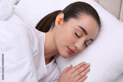 Young woman with foam ear plugs sleeping in bed
