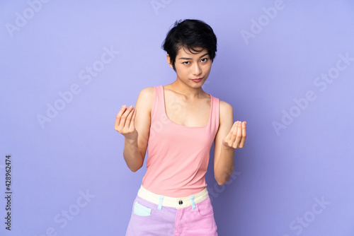 Young Vietnamese woman with short hair over isolated purple background making money gesture but is ruined © luismolinero