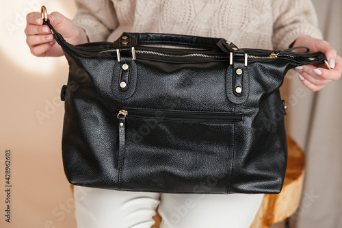 a rectangular black leather bag in the girl's hands. Indoors on a beige background