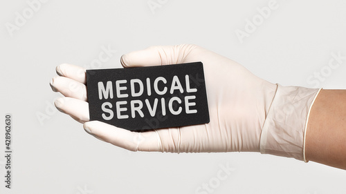 Closeup of the hand in a white sterile glove holding a card with text - medical service