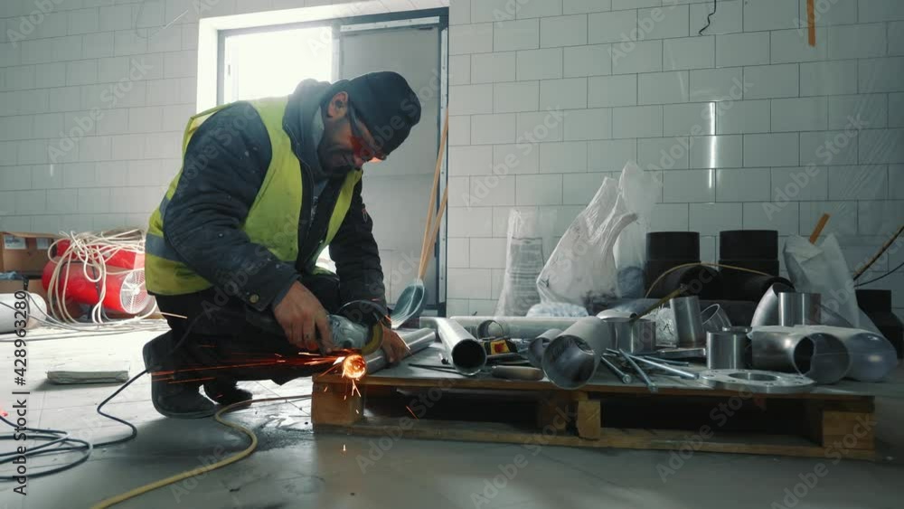 Male locksmith working in production. A man cuts a metal pipe with his hand without protection. Sparks flying off cutting a metal pipe. Male locksmith working in production. A man cuts a metal pipe with his hand without protection. Sparks flying off cutting a metal pipe.