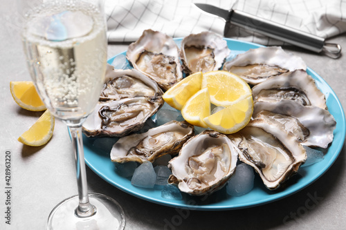 Fresh oysters with lemon and glass of champagne on grey table, closeup
