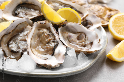 Fresh oysters with lemon on grey table  closeup