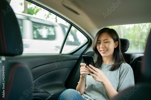 Asian woman sitting in a car is delighted after seeing a message on her cell phone. © Worranan