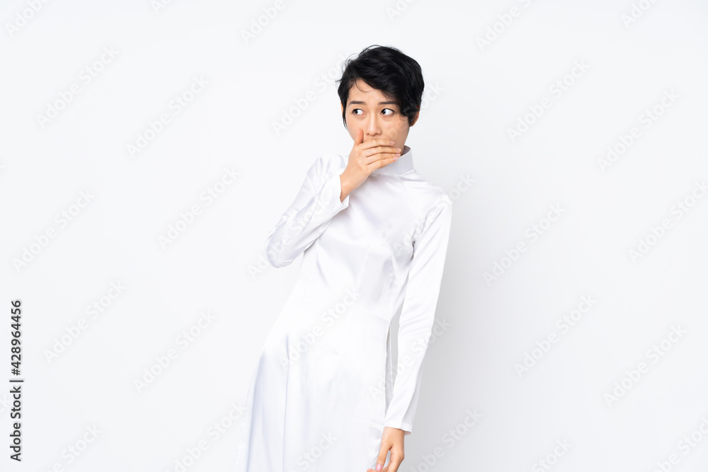 Young Vietnamese woman with short hair wearing a traditional dress over isolated white background doing surprise gesture while looking to the side Young Vietnamese woman with short hair wearing a traditional dress over isolated white background doing surprise gesture while looking to the side
