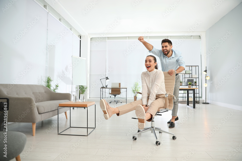 Office employee giving his colleague ride in chair at workplace. Space for text Office employee giving his colleague ride in chair at workplace. Space for text