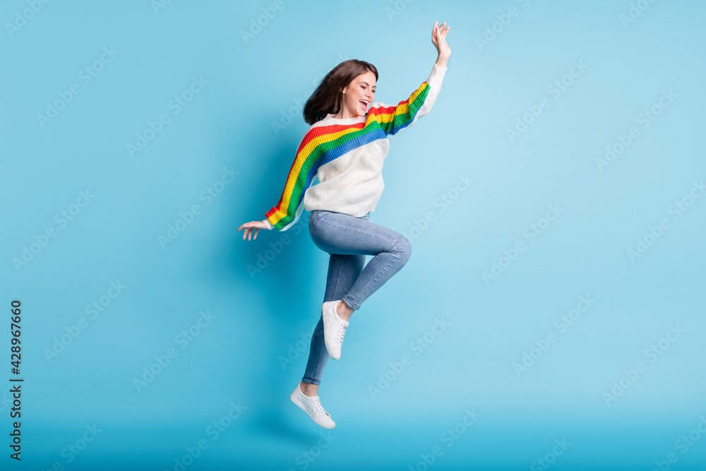 Full length photo of pretty adorable young woman dressed striped sweater jumping high rising arm isolated blue color background