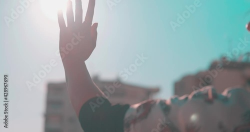 Waving hand to glare of sun flare in afternoon time, urban street. Woman's hand on balcony, sunbeams an gesture.