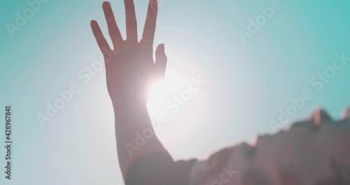 Waving hand to glare of sun flare in afternoon time, urban street. Woman's hand on balcony, sunbeams an gesture.
