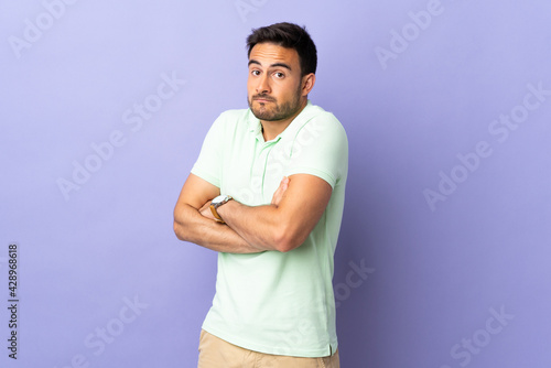 Young handsome man isolated on purple background making doubts gesture while lifting the shoulders
