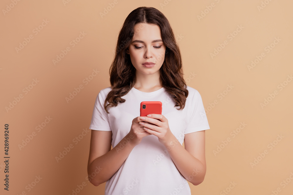Photo of pensive woman hold telephone look screen read sms posing on beige background Photo of pensive woman hold telephone look screen read sms posing on beige background